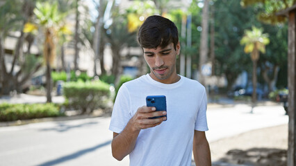 Cool looking young hispanic man, with serious expression, deeply engrossed in texting on smartphone...