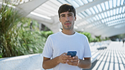 Cool looking young hispanic man, with serious expression, deeply engrossed in texting on smartphone...