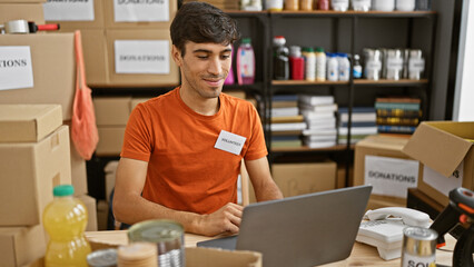 Smiling young hispanic man volunteering at local charity center, sitting with laptop on table