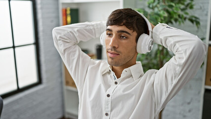 Young hispanic man business worker listening to music relaxed at the office