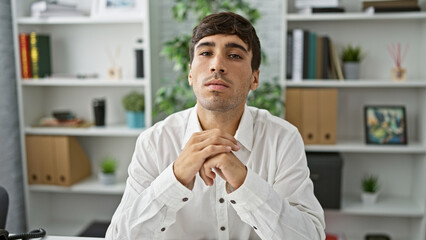 Handsome, young hispanic man sits at office table, embodying confidence. this serious business...