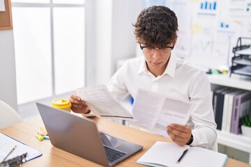 Young hispanic teenager business worker using laptop reading document at office