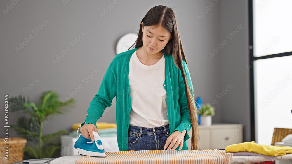 Wall mural Young chinese woman ironing clothes at laundry room - Wall murals