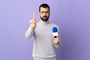 Adult reporter man with beard holding a microphone over isolated purple background counting one...