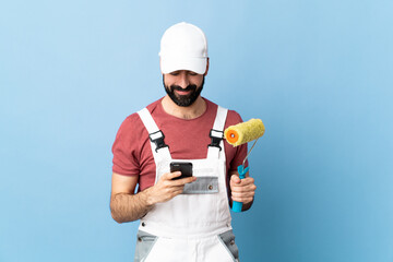 Adult painter man over isolated blue background sending a message with the mobile