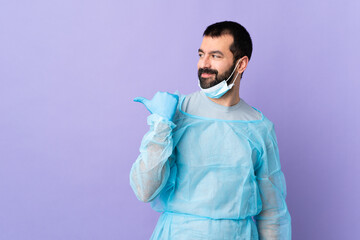 Surgeon man with beard with blue uniform over isolated purple background pointing to the side to present a product