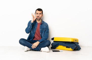 Caucasian handsome man with a suitcase full of clothes sitting on the floor at indoors showing a...