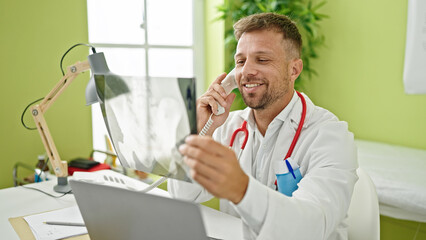 Naklejka na ściany i meble Young man doctor talking on telephone holding xray at clinic