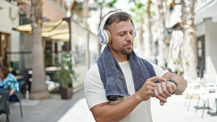 Young man wearing sportswear listening to music looking watch at street