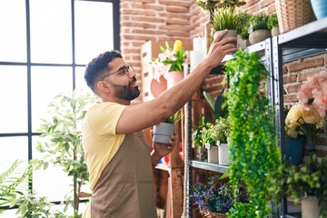 Young arab man florist holding plant standing at florist