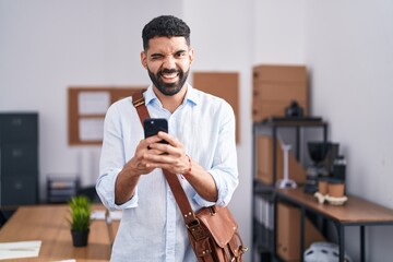 Hispanic man with beard using smartphone at the office winking looking at the camera with sexy...