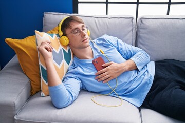 Young caucasian man listening to music sleeping on sofa at home