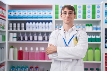Young caucasian man pharmacist smiling confident standing with arms crossed gesture at pharmacy
