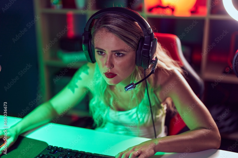 Wall mural Young beautiful hispanic woman streamer playing video game using computer at gaming room