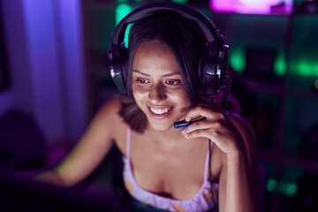 Young hispanic woman streamer smiling confident playing video game at gaming room
