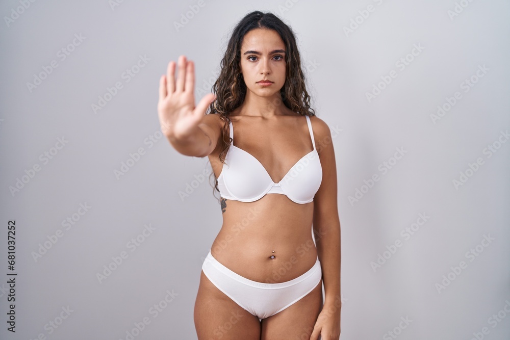 Wall mural young hispanic woman wearing white lingerie doing stop sing with palm of the hand. warning expressio