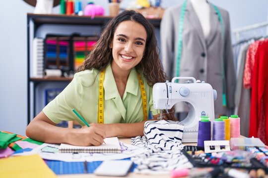 Young beautiful hispanic woman tailor smiling confident drawing on notebook at clothing factory