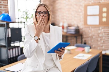 Young caucasian woman working at the office wearing glasses shocked covering mouth with hands for...