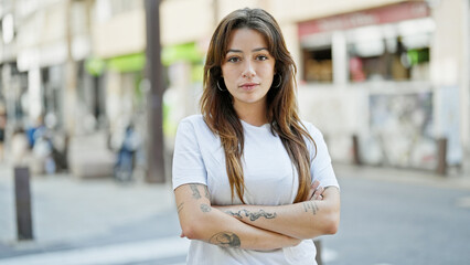 Young beautiful hispanic woman standing with serious expression with arms crossed gesture at street - obrazy, fototapety, plakaty