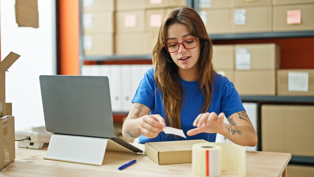 Young beautiful hispanic woman ecommerce business worker putting sticker on package at office