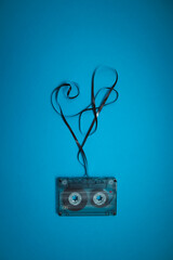 Transparent audio cassette with loose tape on blue background. Place for text.