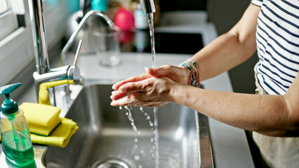 Middle age hispanic woman washing hands at the kitchen