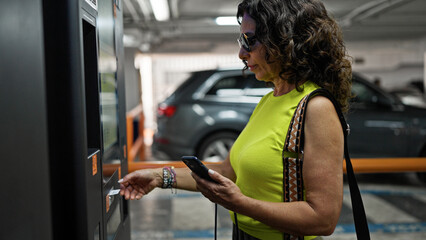 Middle age hispanic woman paying at parking machine parking