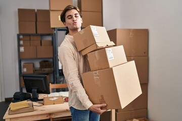 Young man working at small business ecommerce holding packages looking at the camera blowing a kiss being lovely and sexy. love expression.