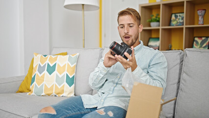 Young caucasian man unpacking camera of cardboard box surprised at home