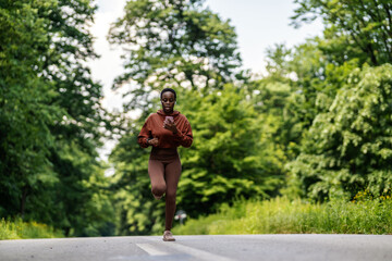 Fototapeta na wymiar One african american female athlete looking focused while out for run to increase her cardio and endurance. A young black woman running outside to increase her speed and pace. Fitness is a lifestyle.