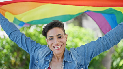 Young beautiful hispanic woman smiling confident holding rainbow flag at park