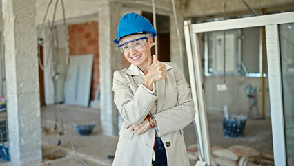 Middle age blonde woman architect standing with arms crossed gesture doing thumb up gesture at construction site