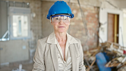 Middle age blonde woman architect standing with relaxed expression at construction site
