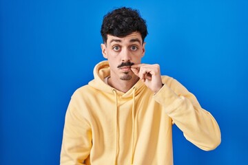 Naklejka premium Hispanic man standing over blue background mouth and lips shut as zip with fingers. secret and silent, taboo talking