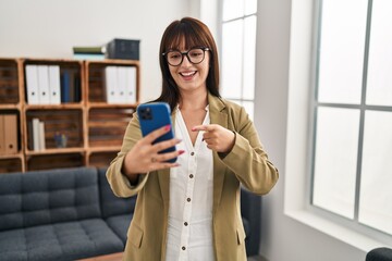 Young brunette woman working at the office with smartphone smiling happy pointing with hand and finger