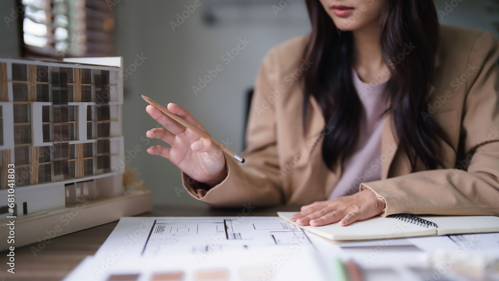 Poster female architect looking on building model and designing architecture interior project on blueprint
