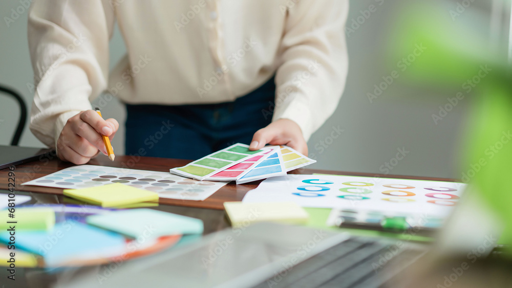 Poster creative graphic designer holding color sample and comparing color swatch on document to designing