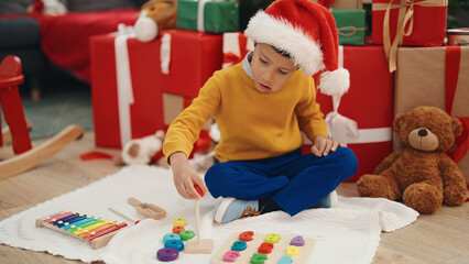 Adorable hispanic boy playing with hoops toy sitting on floor by christmas gifts at home