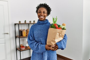 African american woman smiling confident holding groceries bag at home