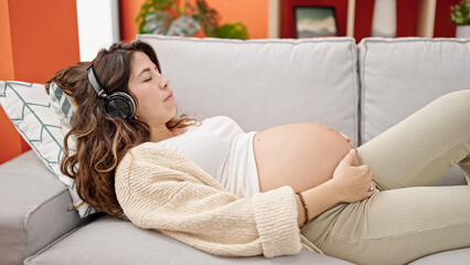Young pregnant woman listening to music sleeping on sofa at home