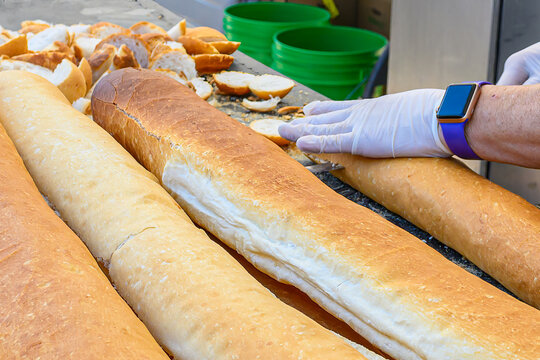 Closeup of Hands Slicing French Bread to Make Poboy Sandwiches  at the 2023 Poboy Festival in New Orleans - Powered by Adobe