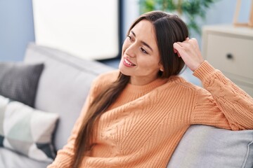 Young beautiful hispanic woman smiling confident sitting on sofa at home