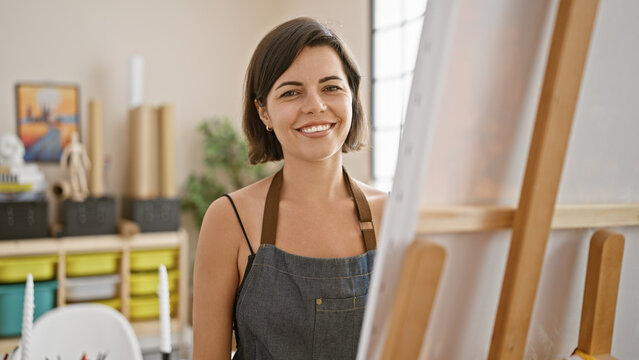 Radiant short-haired hispanic young woman, a confident artist, joyfully drawing in a bustling university art studio