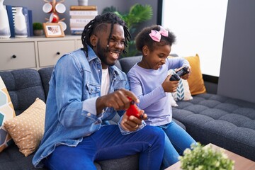 Father and daughter playing video game sitting on sofa at home