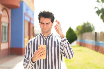 Young handsome man using mobile phone with fingers crossing