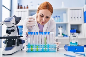 Young caucasian woman scientist pouring liquid on test tubes at laboratory