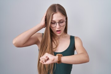 Young caucasian woman standing over white background looking at the watch time worried, afraid of...