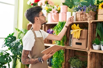 Young hispanic man florist reading notebook with relaxed expression at flower shop