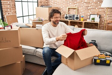 Middle age man smiling confident unpacking cardboard box at new home - Powered by Adobe
