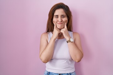 Brunette woman standing over pink background smiling with open mouth, fingers pointing and forcing cheerful smile